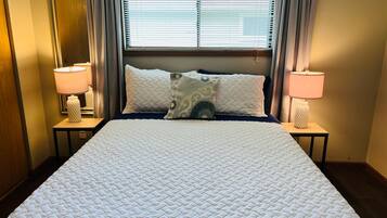 A hotel room with a large bed, two bedside lamps, a window with blinds, and a mirror on the wall.