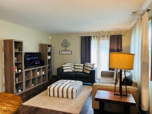 Una sala de estar con sofá, reposapiés, televisor, estantería y lámpara.