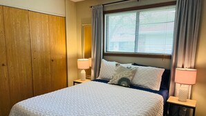 Ein Hotelzimmer mit einem Bett, zwei Nachttischlampen, einem Fenster mit Jalousien und einem Holzschrank.