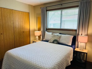 Una habitación de hotel con una cama, dos lámparas de noche, una ventana con persianas y un armario de madera.