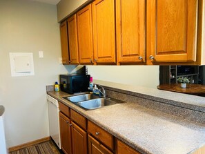 Una cocina con armarios de madera, un lavamanos de acero inoxidable, un microondas y una botella de detergente.