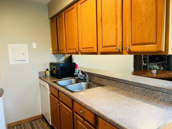 A kitchen with wooden cabinets, a stainless steel sink, a microwave, and a dish soap bottle.