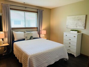 A neatly arranged bedroom with a bed, bedside lamps, a dresser, and a window with curtains.