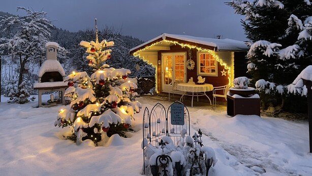 A cozy cabin with a snow-covered exterior, a small outdoor seating area, and a pizza oven. - Holiday apartment Wambach (Kleines Wiesental)