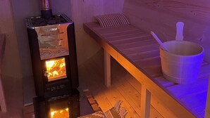 A cozy sauna room with a wood-burning stove, a bench, and a bucket. - Holiday apartment Wambach (Kleines Wiesental)