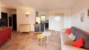 A living room with a sofa, a coffee table, and a TV. There is a kitchen in the background with a sink and cabinets. - Apartments in Residence with swimming pool (Sainte-Lucie de Porto-Vecchio)