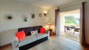A living room with a sofa, a table, and a view of an outdoor patio. - Apartments in Residence with swimming pool (Sainte-Lucie de Porto-Vecchio)