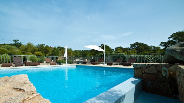 A swimming pool with lounge chairs and umbrellas, surrounded by a stone wall and greenery. - Apartments in Residence with swimming pool (Sainte-Lucie de Porto-Vecchio)