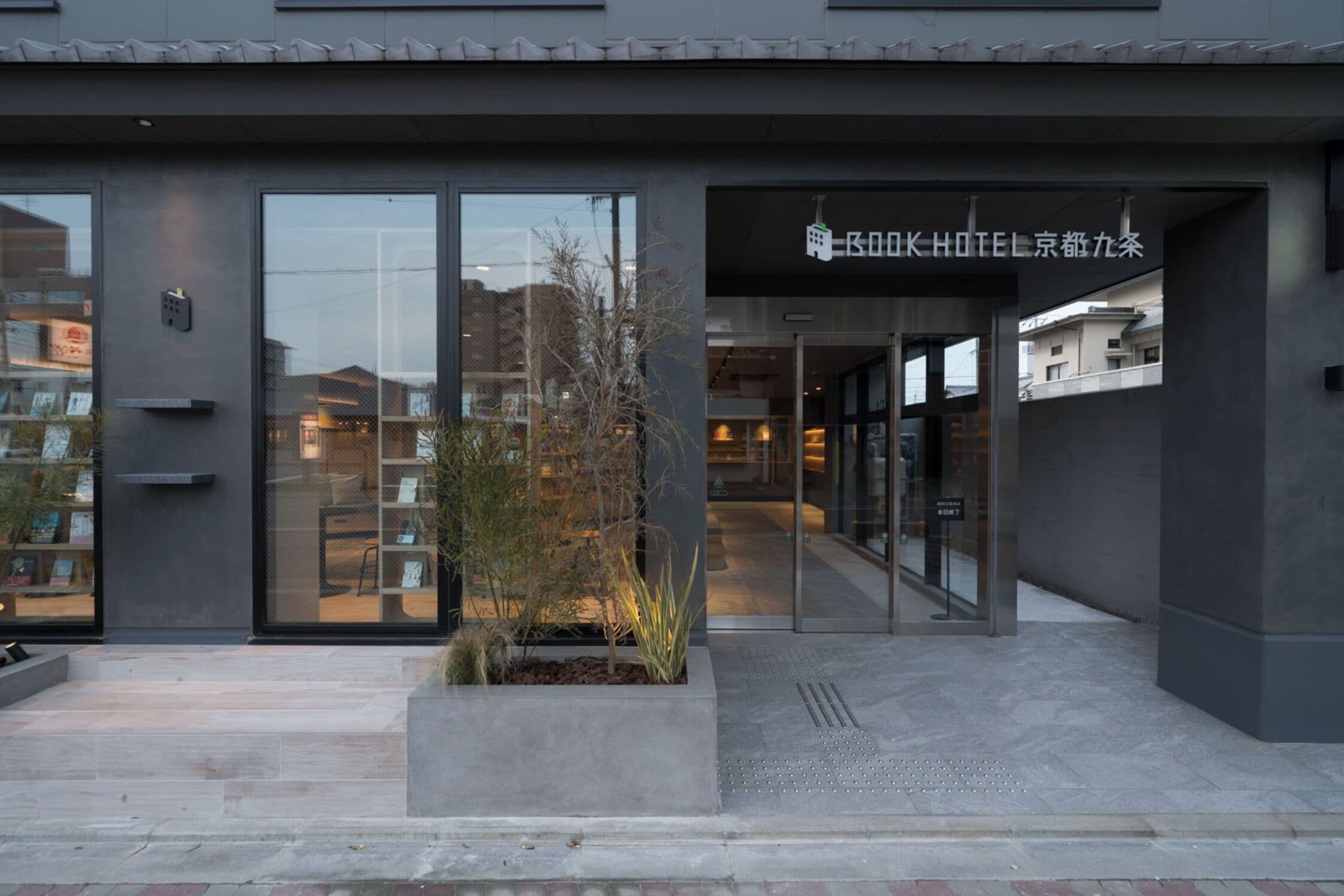 A modern hotel entrance with large glass doors, a small outdoor planter, and a sign above the entrance.