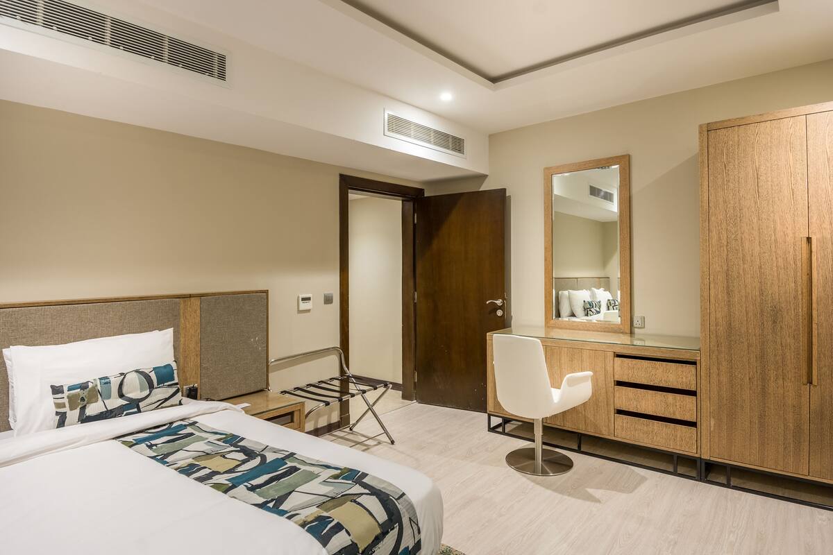 A hotel room with a bed, a desk, a chair, a wardrobe, and a mirror.