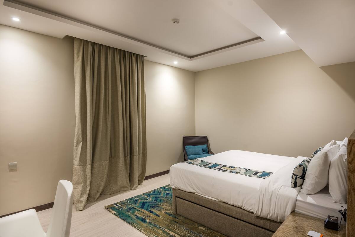 A bedroom with a bed, a chair, a desk, and a large window with curtains.