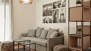 A modern living room with a grey sofa, patterned ottomans, a glass coffee table, and a wooden shelving unit with plants. - Kolonaki Square Executive Apartment (Athens)