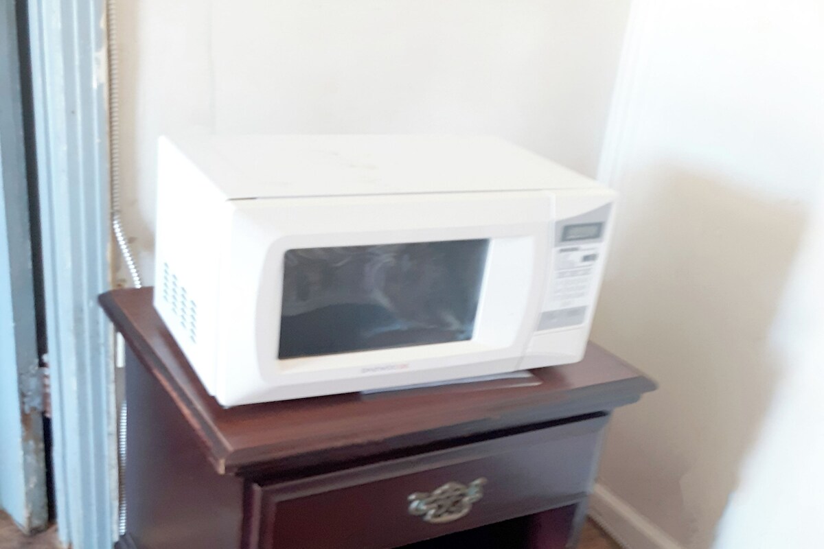 Un four à micro-ondes blanc, posé sur un meuble en bois doté d’un tiroir.