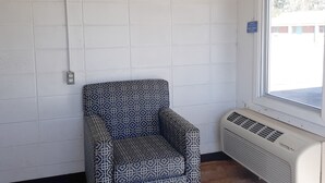 A corner room with a patterned armchair, a window, and a wall-mounted air conditioning unit.