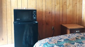 A compact kitchenette with a microwave and a small refrigerator, wooden panel walls, and a patterned bedspread.