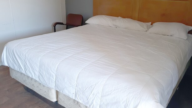 A large bed with a wooden headboard, a chair, and a plain wall.