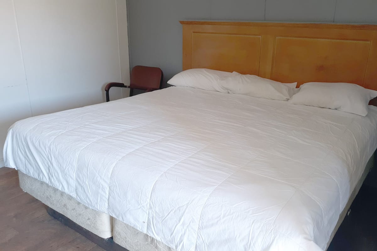 A large bed with a wooden headboard, a chair, and a plain wall.