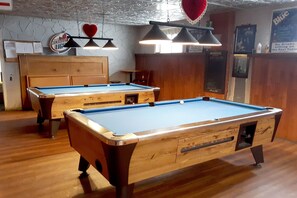 A pool table with a wooden finish and a blue felt surface, accompanied by a smaller table and a wooden cabinet.