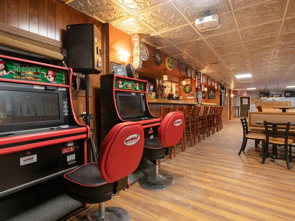 A bar area with arcade machines, wooden flooring, and a bar counter.