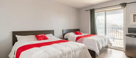 A hotel room with two beds, a large window with a view, and a small kitchenette.