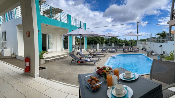A poolside area with lounge chairs, a table with breakfast items, and a clear view of the pool. - Abiki Mauritius (Albion)