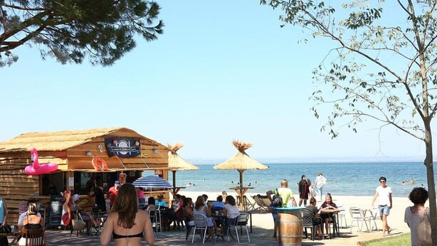 A beachside restaurant with outdoor seating, a wooden structure, and a view of the sea.
