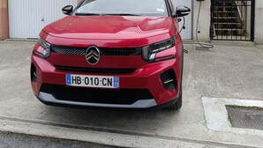 A red car parked in front of a building with a garage door and a staircase.