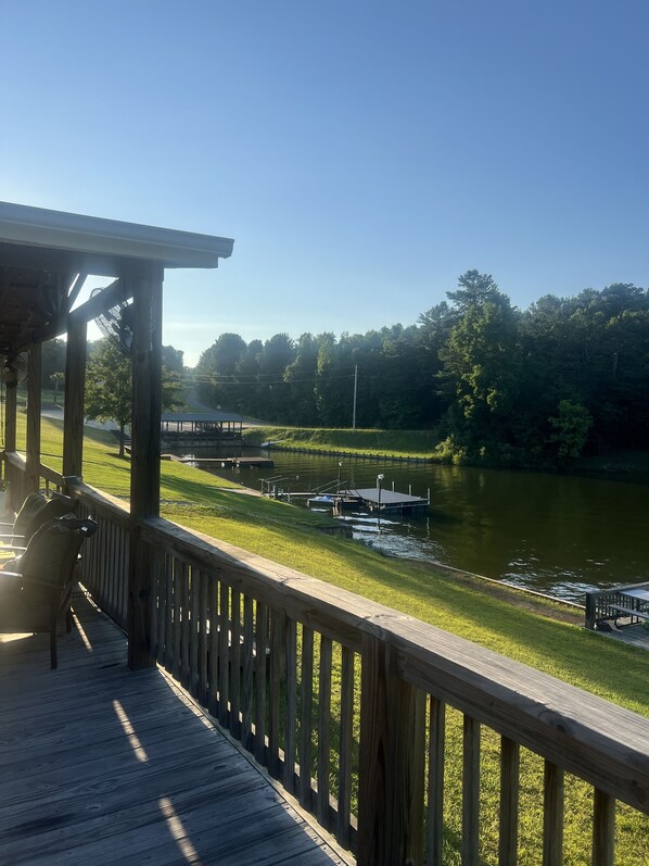 Una terraza de madera con vistas a un río, barcos y una zona con césped.