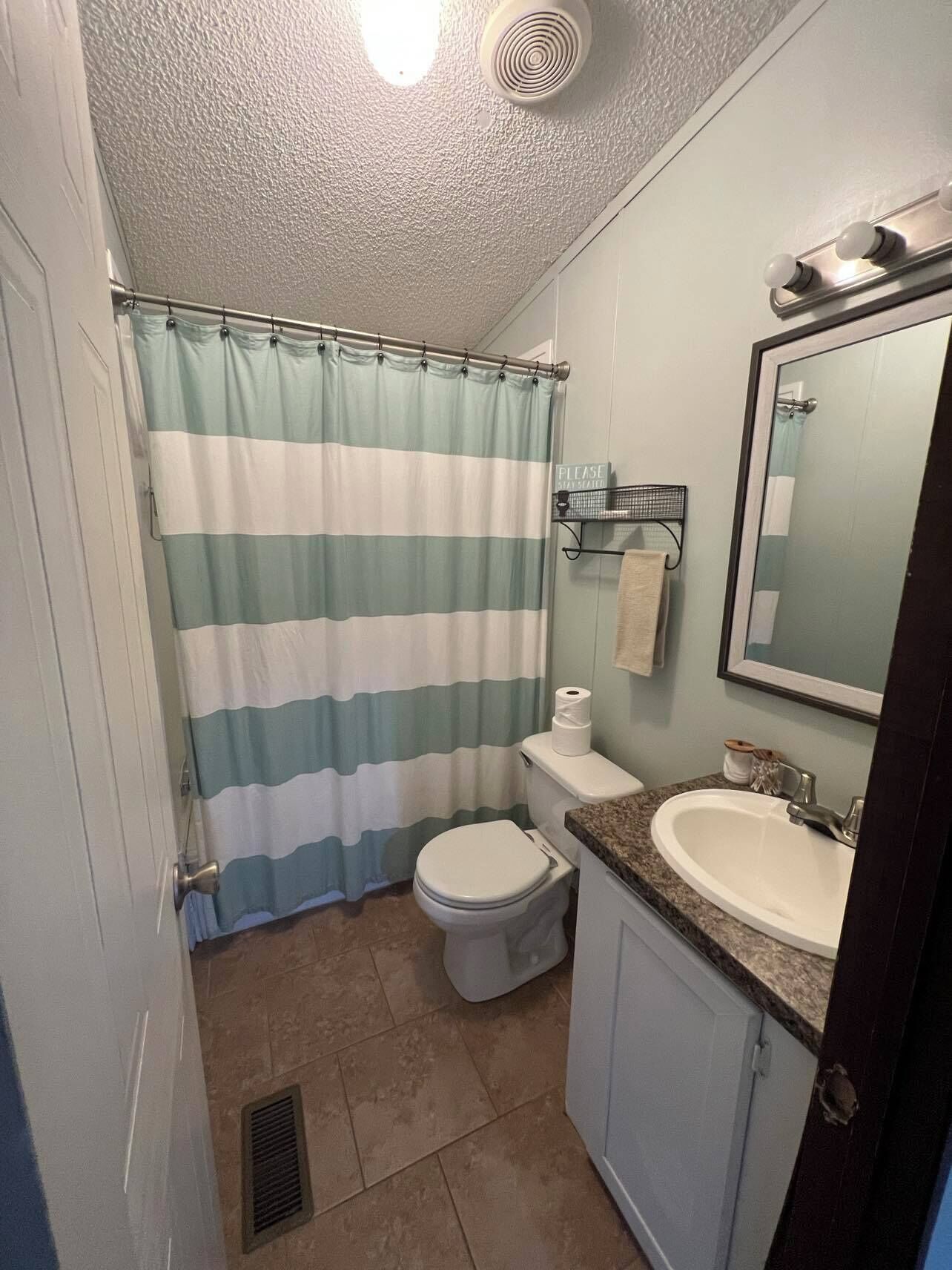 Een badkamer met een kamerjas-effect gordijn, toilet, wastafel en spiegel.