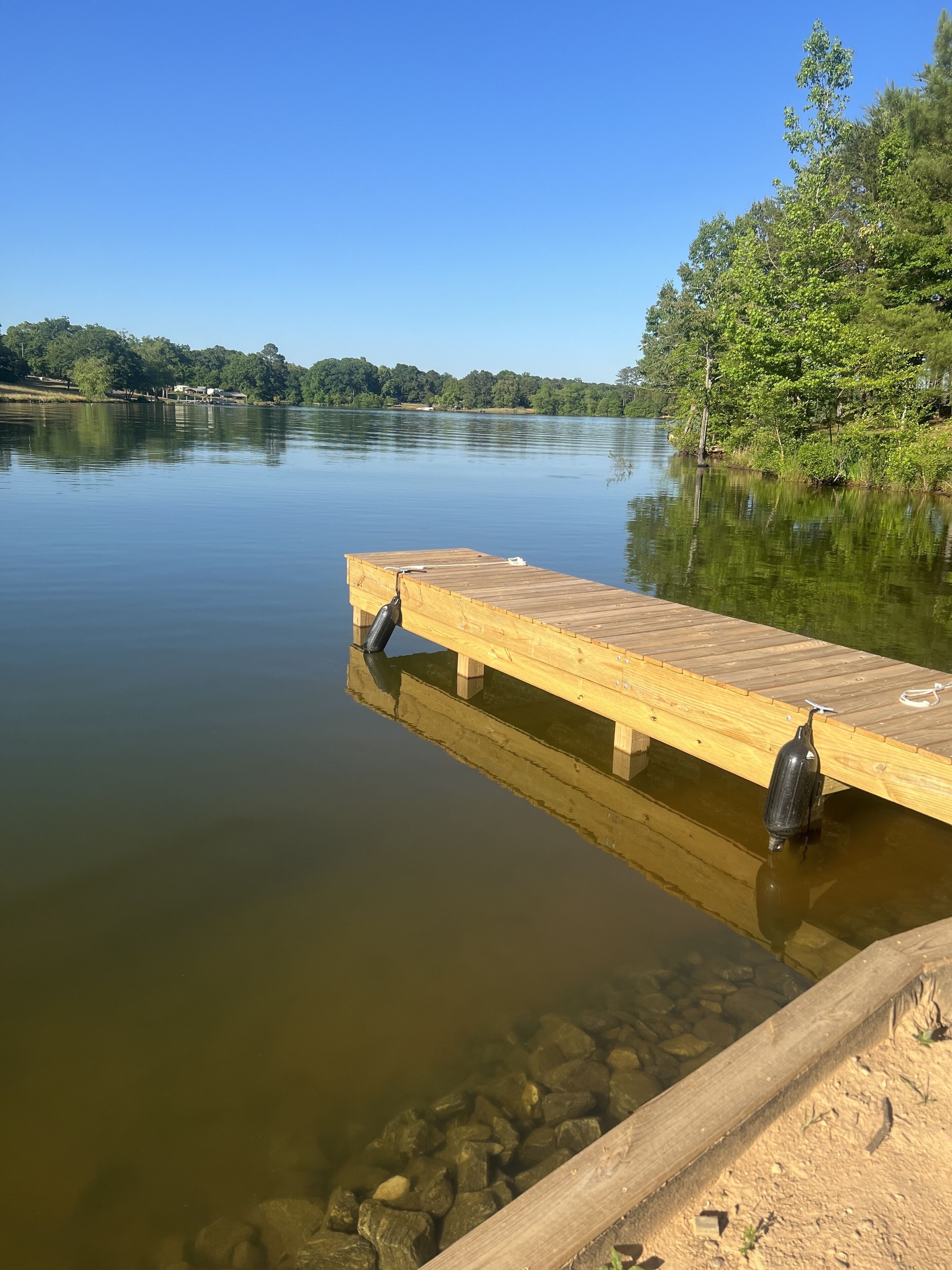 Eine Holzstele, die sich in ruhiges Wasser erstreckt, mit blauem Himmel darüber.