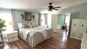 Une chambre spacieuse avec un grand lit, un ventilateur de plafond et un dressing.