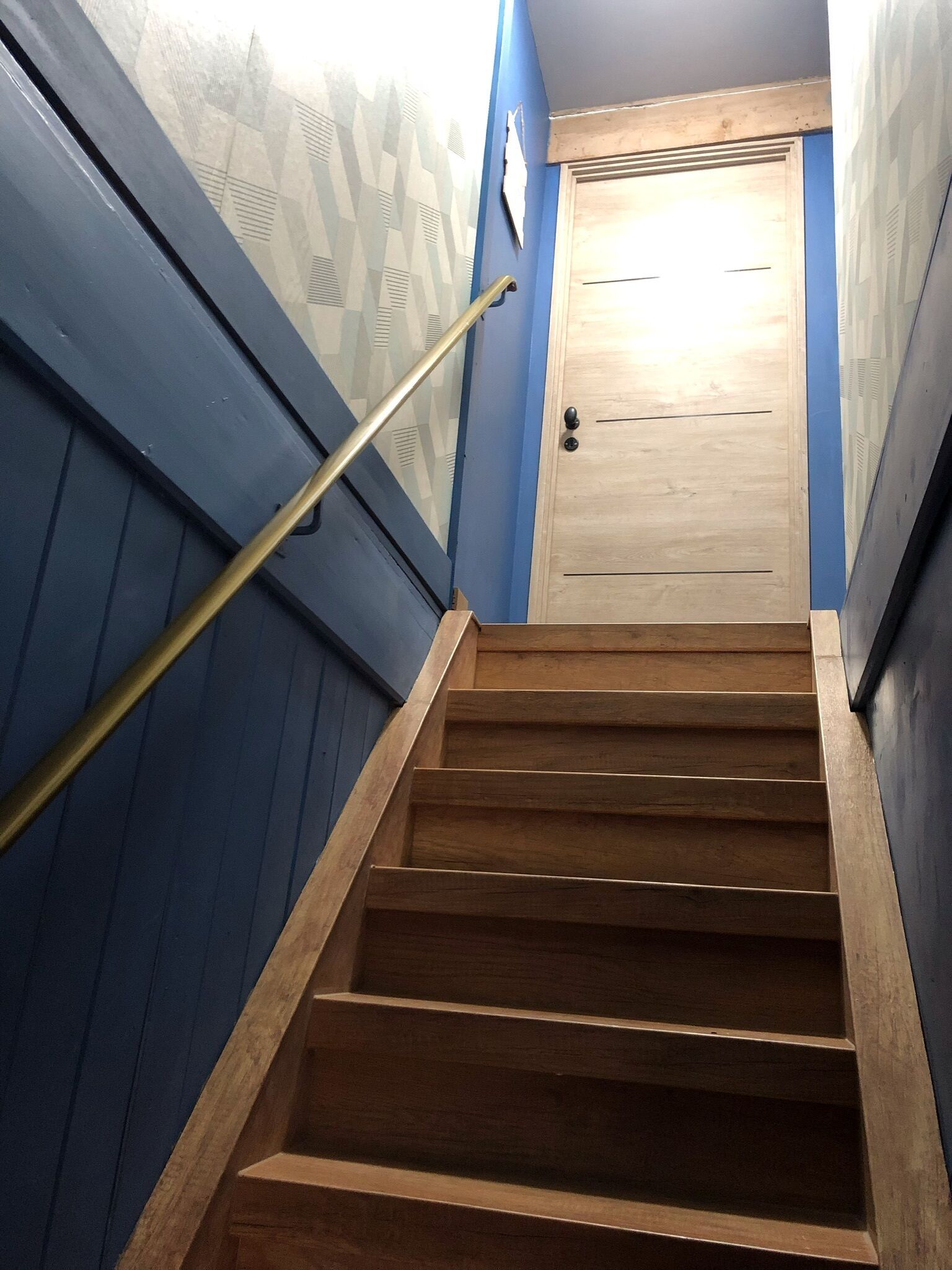 A wooden staircase with a handrail leading to a wooden door.