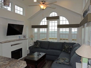 A spacious living room with a large gray sofa, a flat-screen TV mounted on the wall, and a fireplace.