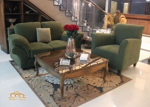 Ein Wohnzimmer mit zwei grünen Sesseln, einem Couchtisch mit einer Rosenvase und einem gemusterten Teppich.