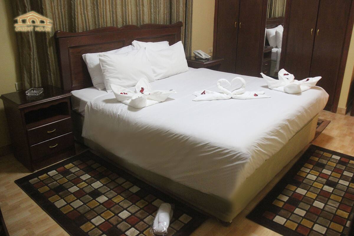 A hotel room with a neatly made bed, a wooden nightstand with a telephone, a mirror, and a small drawer.