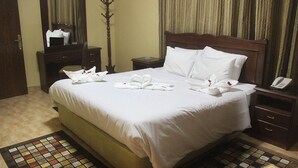 A neatly made bed with white linens and towels arranged in a heart shape, a wooden nightstand with a phone, and a mirror above the dresser. - Orient House Hotel Suites (Amman)