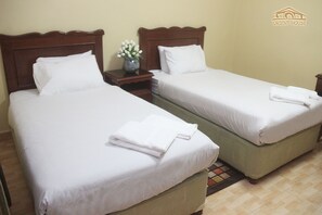 Two single beds with white linens and pillows, a nightstand with a vase of flowers, and a logo on the wall. - Orient House Hotel Suites (Amman)