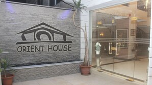 A building facade with a logo reading "ORIENT HOUSE" and a potted plant beside it. - Orient House Hotel Suites (Amman)