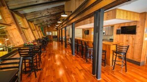 Un espacio alargado y estrecho con pisos y paredes de madera, que incluye una zona central de bar con taburetes y mostrador.
