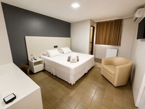 Ein Hotelzimmer mit Bett, Nachttisch, Stuhl und kleinem Schreibtisch mit Telefon.