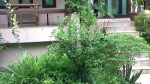 A covered outdoor area with a bench, steps leading to a door, and various plants.