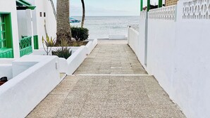 Un étroit sentier pavé menant à une plage, bordé de murs blancs et agrémenté de touches de vert.