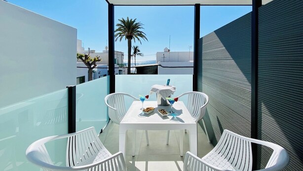 Un espace de restauration extérieur moderne, avec une table et des chaises blanches, offrant une vue sur le paysage urbain et les palmiers.