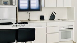 Une cuisine moderne avec des armoires blanches, un four à micro-ondes encastré, un évier, une fenêtre avec des stores, un bloc à couteaux et une paire de lunettes posées sur le comptoir.