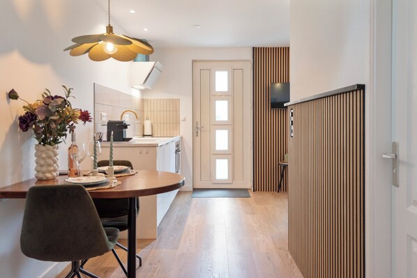 A modern kitchen with a dining area, wooden flooring, and a decorative vase with flowers.