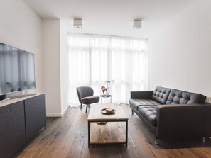 A modern living room with a flat-screen TV, a dark leather sofa, a wooden coffee table, and a black armchair. - Sack-Time 4: Comfortable stay, top location (Zandvoort)