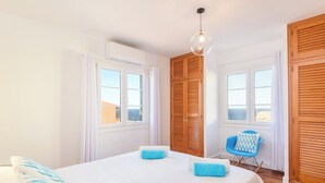 Un dormitorio con dos camas, armarios de madera, una silla y ventanas amplias.