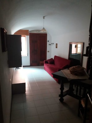 A compact living space with a red sofa, a dining table with a cake, a wooden chair, a television, and a door leading to another room.