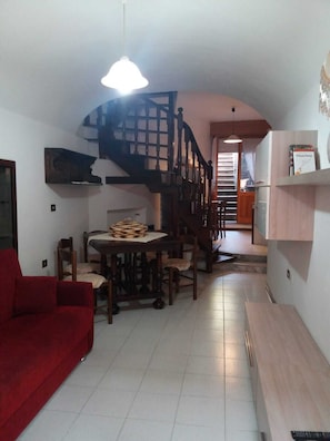 A compact living space with a staircase, a dining area, a red sofa, and a wooden table.