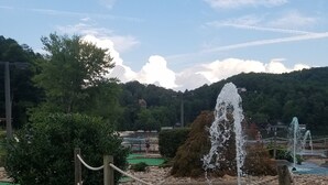 A miniature golf course with a water fountain obstacle, surrounded by greenery and a mountainous backdrop. - The Mountains Win Again (Lake Lure)